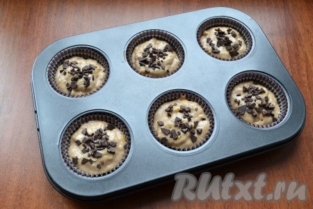 Ячейки формочек для кексов смазать маслом (силиконовые формы можно не смазывать) или вложить в ячейки бумажные формочки. Выложить тесто, заполняя формочки на 2/3 объёма. Дополнительно можно посыпать сверху кексы рубленым шоколадом.