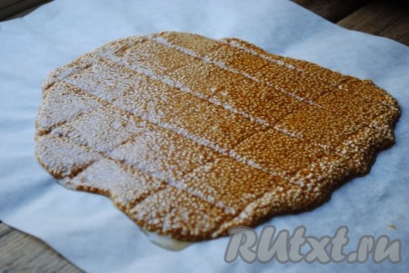 На стол положить лист пергамента и вылить на него грильяжную массу. Накрыть вторым листом пергамента и прокатать скалкой. Это нужно делать быстро, пока кунжутный грильяж не начал застывать.&nbsp;Толщина пласта - не более 3-4 мм. Пока пласт ещё мягкий, нужно ножом нанести насечки, по которым потом будем разрезать конфеты. 