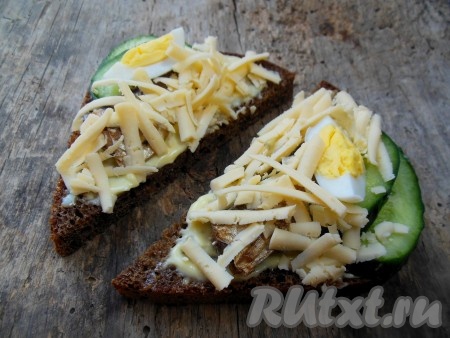 Бутерброды со шпротами, яйцом и огурцом посыпьте натертым сыром.
