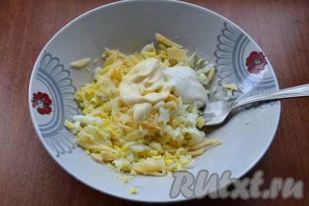 Сыр и вареные яйца натереть на крупной терке, добавить измельченный чеснок, соль, перец, оставшийся майонез и сметану, тщательно перемешать.
