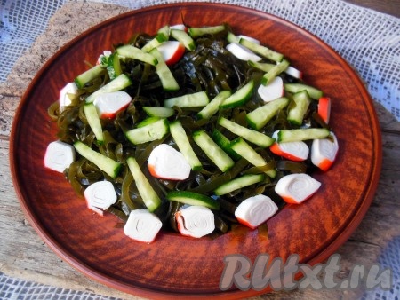 Сверху на капусту разложите нарезанные крабовые палочки и огурцы.