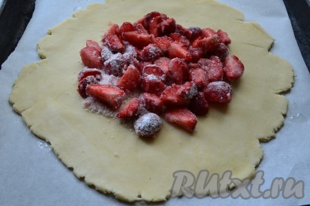 Охладившееся тесто раскатать в лепёшку толщиной около 0,5 сантиметра, выложить её на противень, застеленный пергаментом (если не уверены в качестве пергамента, тогда перед выкладыванием теста смажьте пергамент немного растительным маслом). В середину лепёшки выложить клубнику.