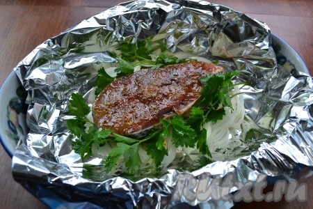 На лук выложить подготовленный стейк толстолобика. По бокам разместить веточки петрушки.
