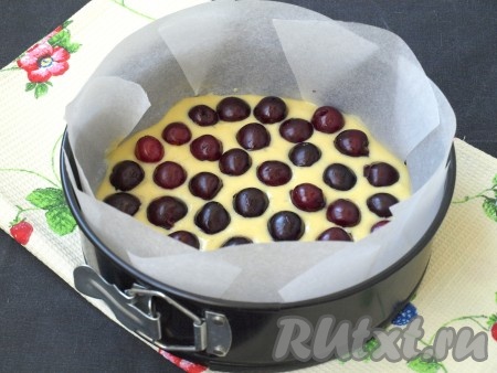 Из черешни удалить косточки. Если ягоды крупные, то можно разрезать пополам. Форму (у меня форма диаметром 22 см) застелить пергаментом, налить на дно немного теста. Поверх теста разложить черешню.
