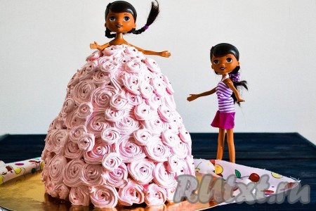 Куклу раздеть, обмотать пищевой пленкой и вставить в подготовленное отверстие. В кондитерский мешок с насадкой "звезда" выложить крем и украсить "платье". Необходимо начать украшать с подола платья и подниматься вверх. Формируя каждую "розочку" на платье, крем нужно выдавливать, начиная от центра и продолжать по кругу и до края. По желанию, в центр каждой "розочки" можно вставить по пищевой бусинке.