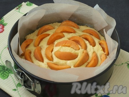 Застелить форму пергаментом и выложить тесто, разровнять поверхность. Абрикосы вымыть и обсушить, нарезать каждый на 4-6 частей, в зависимости от размера плодов. Ломтики абрикосов разместить на поверхности теста, немного вдавливая.