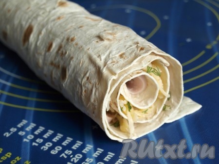 Аккуратно свернуть лаваш в рулет, начиная от края с начинкой. Формировать рулет нужно достаточно быстро, пока он не успел размокнуть. Сырое яйцо взбить вилкой в небольшой ёмкости до однородности. Свободный край лаваша и поверхность рулета со всех сторон смазать взбитым яйцом. Переложить подготовленный рулет на противень, застеленный пергаментом.
