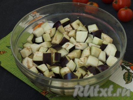 Баклажаны нарезать крупными кубиками. Налить в миску 1 литр воды и добавить 1 столовую ложку каменной соли, размешать. Поместить в эту воду баклажаны, накрыть тарелкой, поставить сверху груз и оставить на 25-30 минут.