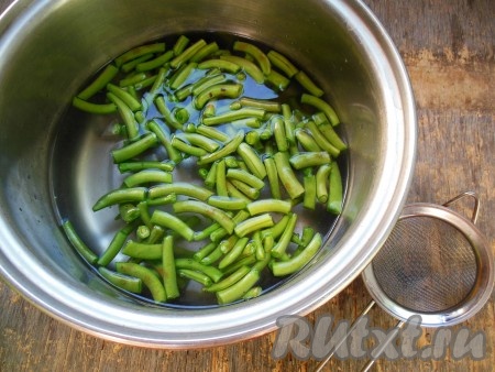 Чтобы фасоль сохранила свой приятный зеленый цвет, ее необходимо бланшировать: в кастрюле вскипятите 1 литр воды, добавьте соль, частями выкладывайте фасоль в кипящую воду, после закипания уменьшите огонь и варите 2 минуты.
