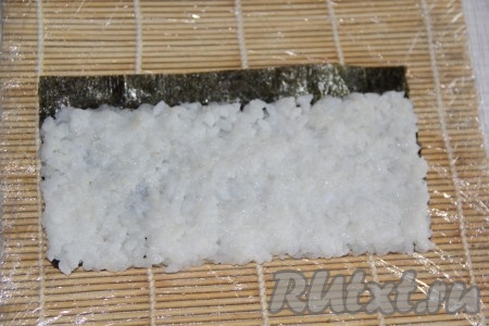 Теперь приступим к формовке наших роллов с омлетом. Разрезать листы нори на две части. На подготовленную циновку выложить лист нори блестящей стороной вниз. Затем выложить небольшую часть риса и разровнять его по поверхности листа нори, оставив свободный край (примерно, 1 см). 