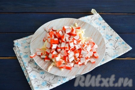 Крабовые палочки нарезать мелкими кубиками и выложить к сыру и чесноку.
