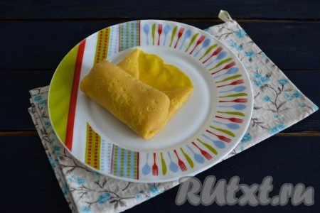 Свернуть яичный блинчик с начинкой конвертиком - для этого нужно вначале завернуть немного края на начинку, а затем свернуть трубочкой.