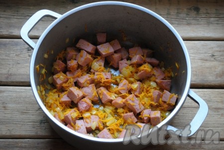В кастрюлю с толстым дном или казанок влить растительное масло и хорошо его разогреть. Обжарить лук с морковкой на среднем огне до золотистого цвета (около 5 минут), периодически помешивая. Затем добавить колбасу и обжарить всё вместе ещё 2-3 минуты. 
