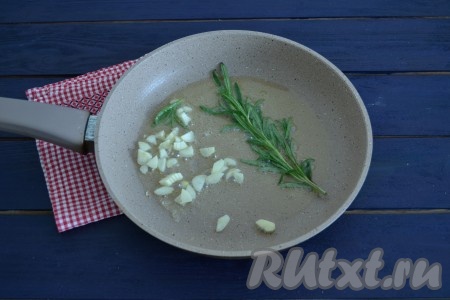 На чистую сковороду влить растительное масло, немного прогреть и выложить пластинами нарезанный чеснок и веточку розмарина.
