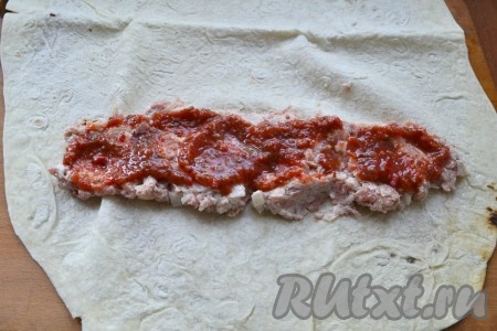 На край лаваша, по всей ширине, выложить фарш, сверху смазать аджикой или томатным соусом.