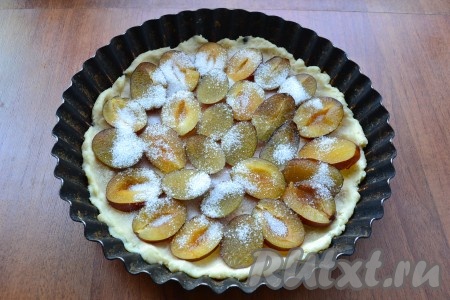 Затем тесто разделить на 2 части. Одну часть поместить на 30 минут в морозилку, другую - в круглой форме растянуть руками в виде лепешки с бортиками. Сливы освободить от косточек, нарезать тонкими пластинами и разместить на тесто. Посыпать сливы 3 столовыми ложками сахара.
