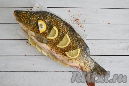 Лимон вымыть и нарезать полукольцами. Половину нарезанного лимона выложить в брюшко, а половину - сверху карпа (на кожицу).
