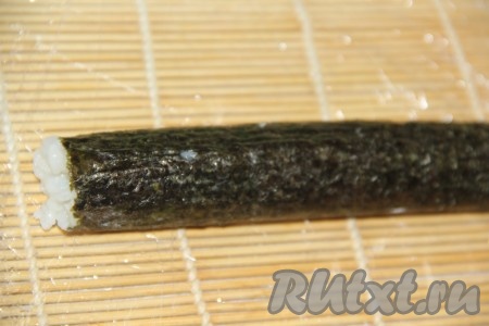 С помощью циновки свернуть рис с начинкой в плотный ролл.