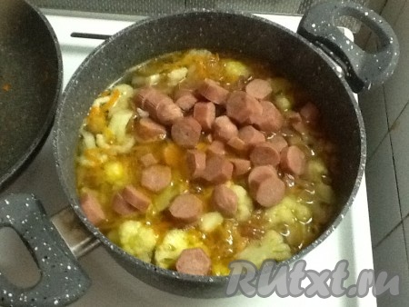 Нарезаем сосиски колечками и отправляем в кастрюлю к овощам.