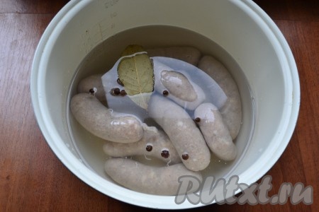 Сардельки наколоть иголкой в нескольких местах и выложить их в чашу мультиварки или кастрюлю. Залить холодной водой, добавить лавровый листик и душистый перец.
