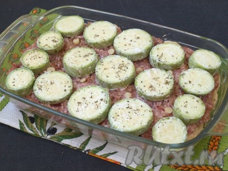 Кружочками нарезать кабачки (молодые кабачки можно не очищать от кожуры и семечек), смешать их с небольшим количеством сметаны, разложить поверх фарша и посыпать прованскими травами. В промежутках разместить кусочки чеснока. Форму накрыть фольгой и поставить в разогретую до 180 градусов духовку.