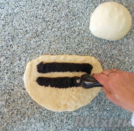 Готовое дрожжевое тесто делим на два равных кусочка (для двух будущих рулетов). На смазанном растительном маслом столе каждый кусочек растягиваем руками (не скалкой!), толщина теста должна составлять, примерно, 1 см. Затем берём готовую маковую начинку. Я использовала маковую начинку ТМ SantaVita Bakers. Готовая маковая начинка значительно упрощает и ускоряет процесс приготовления рулета. Моя готовая маковая начинка по форме напоминает небольшую «колбаску». В упаковке делаем небольшой надрез с краю (примерно 1-1,5 см) и выдавливаем из пакетика мак сразу на подготовленное основание рулета (как на фото). На один рулет уходит, примерно, половина пакетика начинки.
