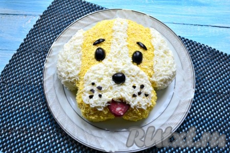 Также оставшимся натертым на мелкой терке белком сделать белую полосочку на мордочке и носик. Разрезанную пополам маслинку выложить в виде глаз и целую маслину - в виде носика. Бровки и усики также вырезать из маслин. Язычок собачки можно сделать из ломтика копченой колбасы.
