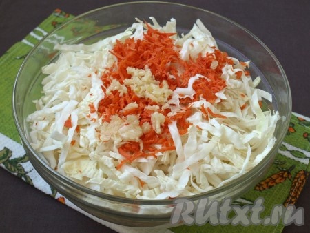 К капусте добавить очищенную и натёртую морковь, выдавить через пресс чеснок, перемешать.
