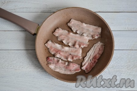 Хорошо разогреть сковороду и выложить в нее тонкие полоски бекона. Масло добавлять не нужно, при нагревании сальная прослойка бекона начинает выделять жир, которого будет достаточно для приготовления яичницы.