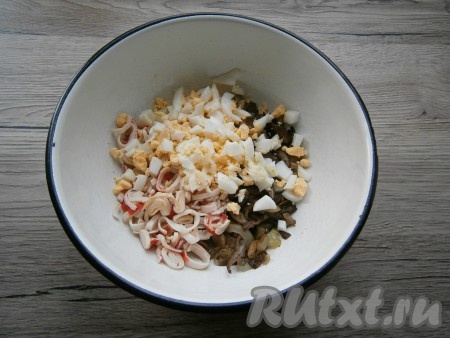 Нарезанные вареные яйца и мелко нарезанный чеснок добавить в салат из жареных крабовых палочек и грибов.
