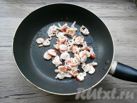 Жарить крабовые палочки, постоянно помешивая, до тех пор, пока большая их часть не раскрутится. В процессе обжаривания палочки немного подрумянятся.
