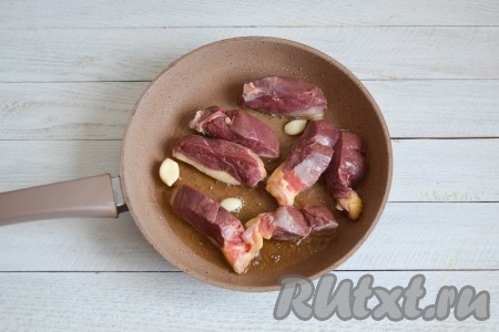 Хорошо разогреть сковороду и выложить кусочки мяса кожицей вниз. Через 1-2 минуты выложить в сковороду очищенные зубчики чеснока. 