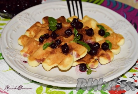 Готовые вафли достать, выложить на тарелку для порционной подачи и остудить. Полить вафли сиропом от варенья вместе с ягодами и подать, украсив листочками мяты к кофе или чаю.
