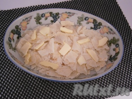 В форму для запекания выложить первым слоем один лаваш, порванный на небольшие части. Сверху лаваша разместить кусочки сливочного масла.
