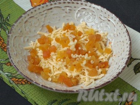 Взять другую тарелку, натереть в неё на крупной тёрке сыр, добавить к нему нарезанную на кубики курагу и 1 измельчённый зубчик чеснока, перемешать.