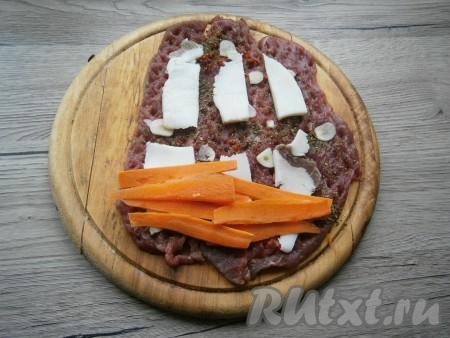 Также выложить сверху мяса тонкие ломтики свиного сала. На краю пласта говядины расположить 5-6 длинных, тонких брусочков сырой моркови.