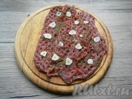 Сложить мясо внахлест, посыпать специями и солью, выложить тонкие ломтики чеснока.