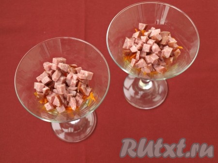 На дно креманок или бокалов выложить морковь по-корейски (если полоски моркови длинные, их можно разрезать на несколько частей). Копчёную колбасу нарезать кубиками и выложить сверху, нанести майонез.