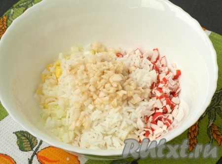 Очищенное яблоко, нарезанное кубиками, и вареный рис выложить в салат из крабовых палочек, лука и яиц.