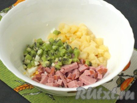 Кубиками нарезать ананасы. Один киви оставить для украшения, а два киви, очистив от кожуры, нарезать кубиками. Ананасы и киви выложить в салат из яиц и ветчины.