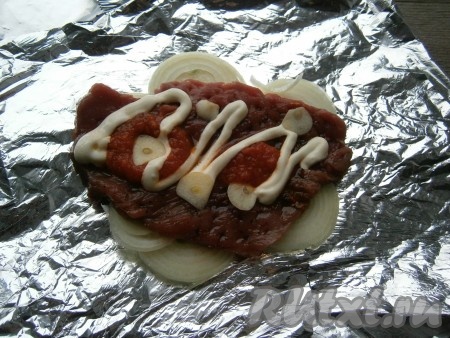 Лук и чеснок очистить. Лист фольги сложить вдвое, на фольгу выложить 1 луковицу, нарезанную кружочками. На лук поместить 1 отбивную из говядины, смазать мясо острым томатным соусом, выложить на него по несколько пластинок чеснока и сверху - сметану или майонез. 