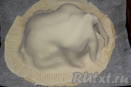Вторую часть теста раскатать в пласт так, чтобы тесто полностью покрыло курочку. Выложить тесто поверх курицы и скрепить края теста с помощью вилки.
