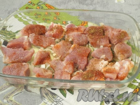 Смазать форму для запекания растительным маслом. Очищенный лук нарезать полукольцами и выложить на дно формы, сверху разложить свинину, посолить и поперчить, по желанию, посыпать мясной приправой.

