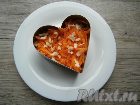 Далее выложить очищенную сырую морковь, натертую на крупной терке, разложить очищенный измельченный чеснок, немного подсолить.
