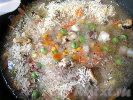 Затем высыпать промытый рис, специи, травы и залить водой в количестве на 1,5 - 2 см выше уровня риса с овощами и морепродуктами.