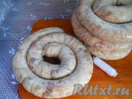 Аналогично наполните свиные кишки оставшимся фаршем. Получившиеся колечки колбасы перевяжите нитками (как на фото), чтобы при варке они не распались.
