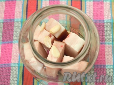 Сало поместить в банку вертикально. Крупными пластинками нарезать очищенный чеснок и добавить в банку.
