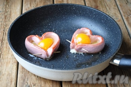 Аккуратно, чтобы не повредить желток, вбить внутрь каждого "сердца" по одному яйцу. Яичницу посолить по вкусу. Если яичный белок немного растечётся по сковороде - ничего страшного, перед подачей его можно убрать.&nbsp;Накрыть сковороду крышкой и готовить на небольшом огне около 5 минут (до готовности яйца). Время приготовления будет зависеть от ваших вкусовых предпочтений: если хотите получить более жидкий желток - хватит и 3-5 минут, если полностью приготовленный - жарить около 7 минут.
