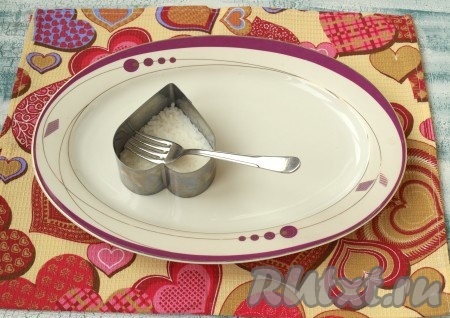 На плоскую тарелку поставить формочку в виде перевёрнутого сердца и выложить в неё отварной рис, смазать майонезом. Все продукты, кроме икры, разделите на 2 части - так вы будете сразу видеть, сколько у вас пойдёт на одно сердечко. Одно сердечко у нас будет женское, а второе - мужское. Если есть 2 формочки, то можно сразу выполнять 2 части салата. Все слои промазывать майонезом и прижимать вилкой.
