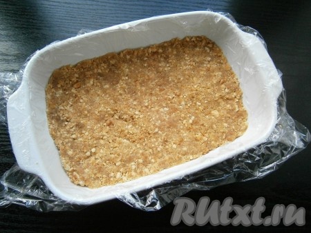 Небольшую прямоугольную форму (размер моей формы 17х12 см) застелить пищевой пленкой, выложить крошку из печенья с маслом, разровнять и утрамбовать. Поместить форму в морозилку на 15 минут.
